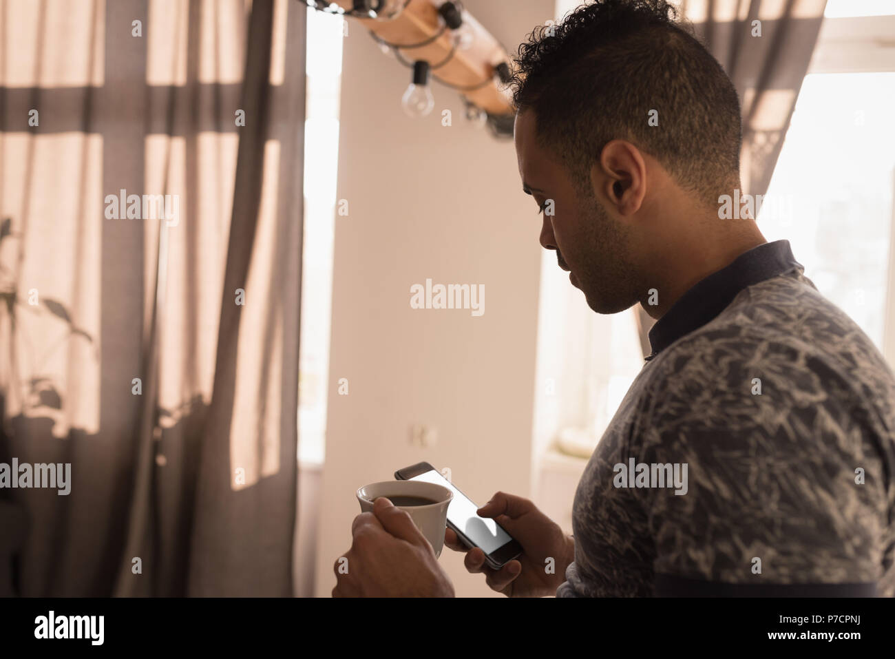 Man using mobile phone while having coffee in kitchen Stock Photo