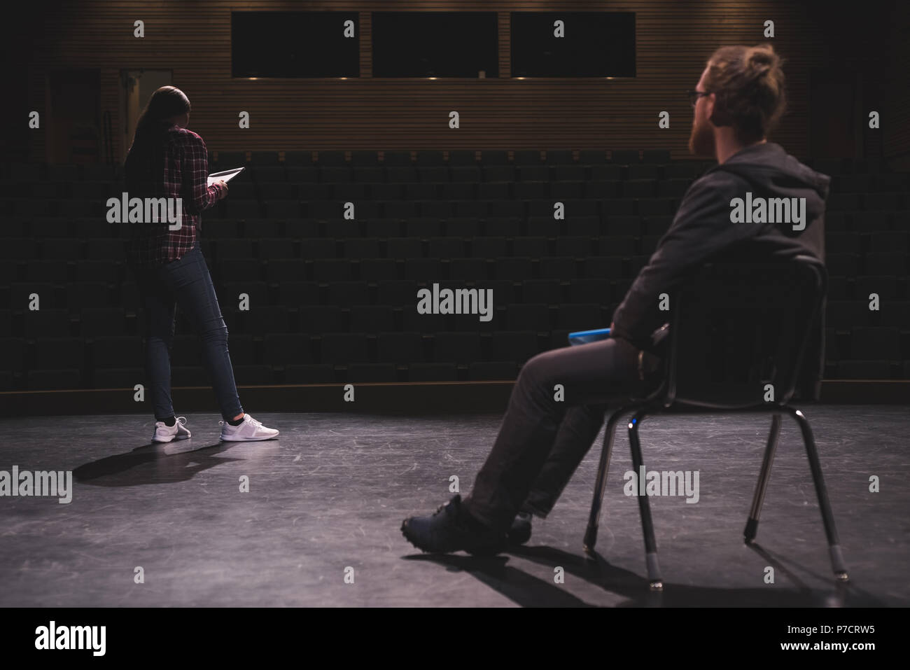 Female actress reading script while male actor looking at her on stage Stock Photo