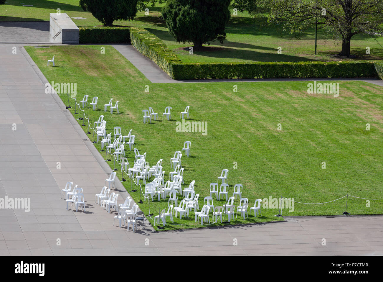 White plastic outdoor chairs on grass near walkway on bright sunny day Stock Photo