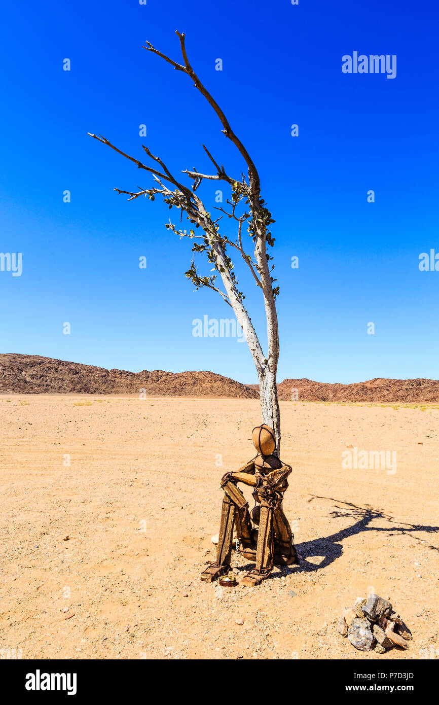 Cairn Lonely Man sits under a dried-up tree in Hartmann Valley, Kunene region, Namibia Stock Photo