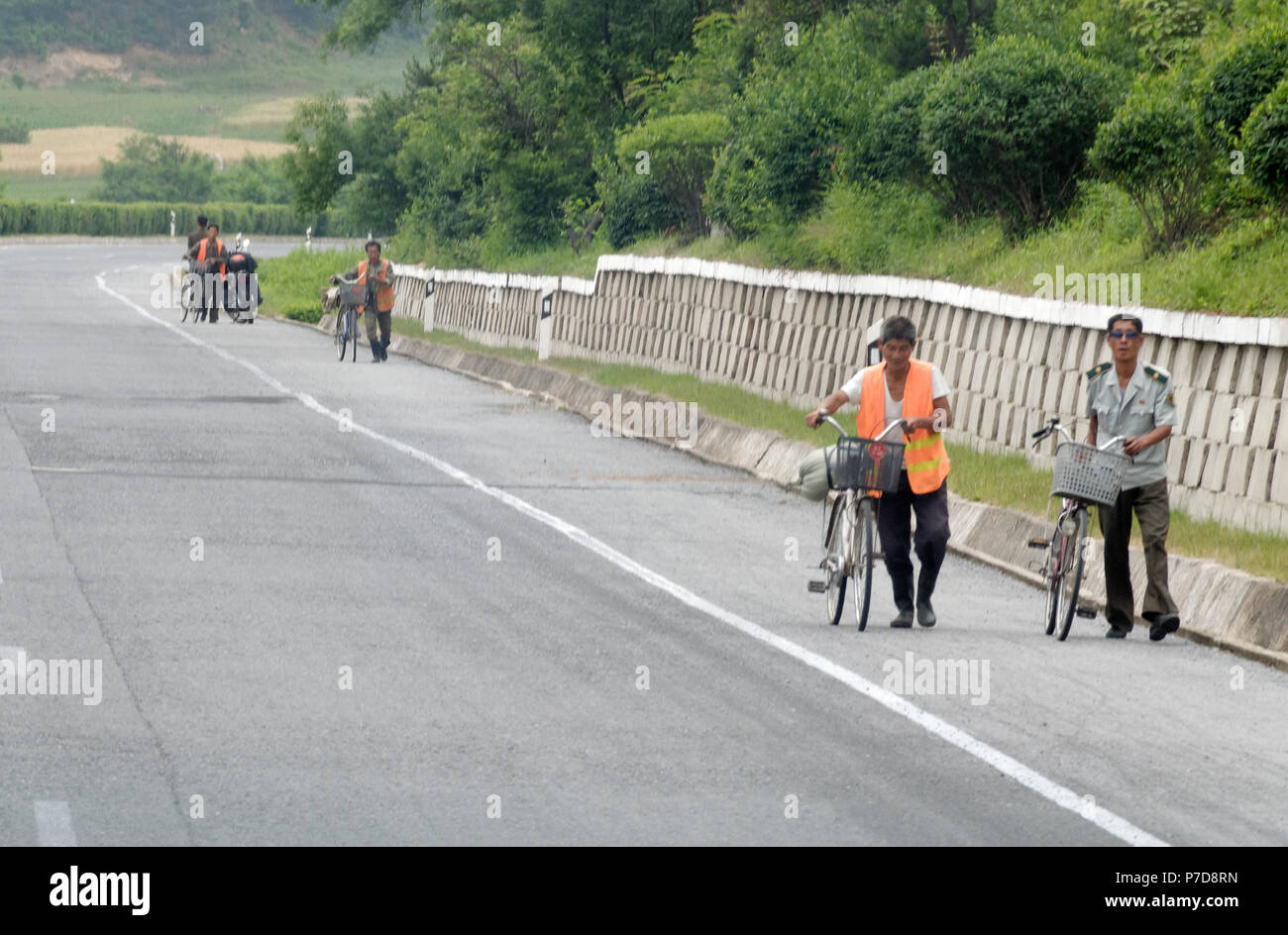 North Korean men pushing bicycles along the hard shoulder reservation of an empty motorway the Kaesong highway south of Pyongyang, North Korea Stock Photo