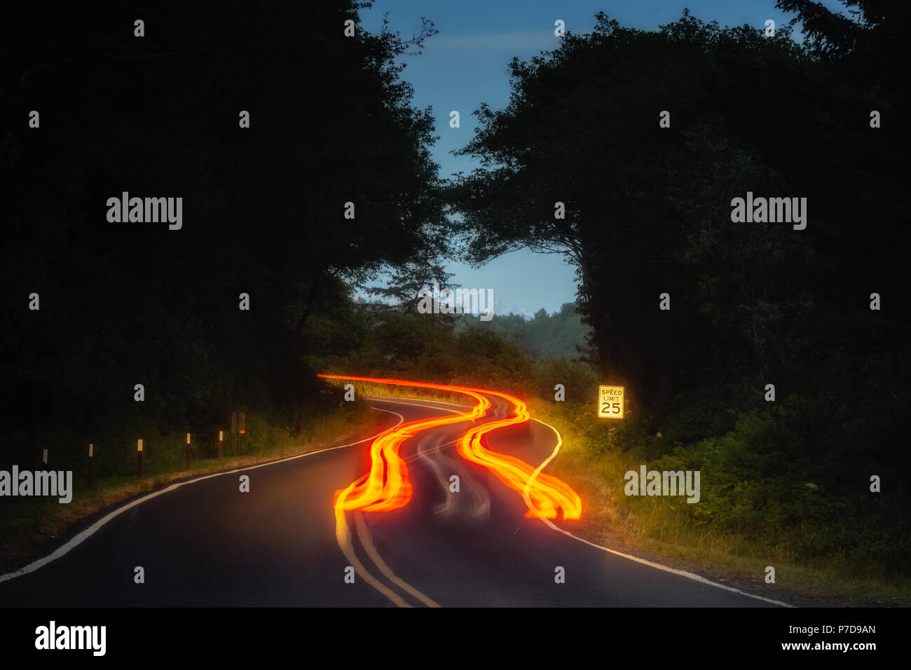 Car tail light trails on a winding road at night in forest. Stock Photo
