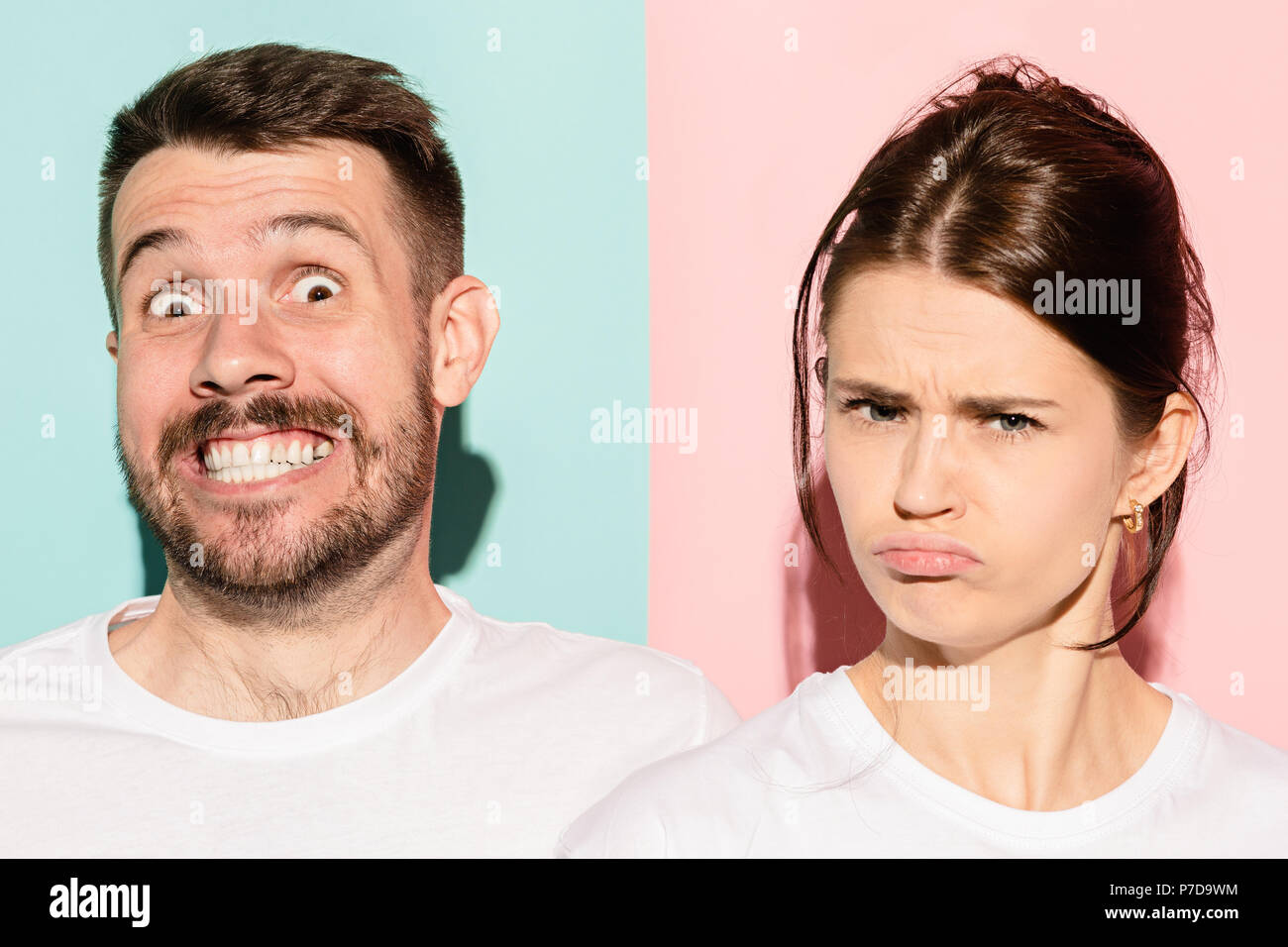 Closeup portrait of young couple, man, woman. One being excited happy smiling, other serious, concerned, unhappy on pink and blue background. Emotion contrasts Stock Photo