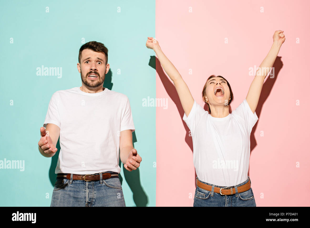 Closeup portrait of young couple, man, woman. One being excited happy smiling, other serious, concerned, unhappy on pink and blue background. Emotion contrasts Stock Photo