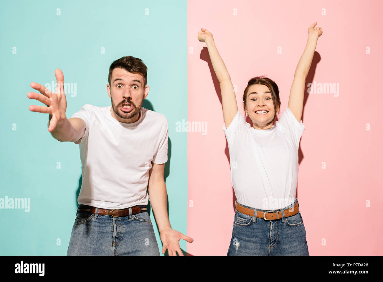 Closeup portrait of young couple, man, woman. One being excited happy smiling, other serious, concerned, unhappy on pink and blue background. Emotion contrasts Stock Photo