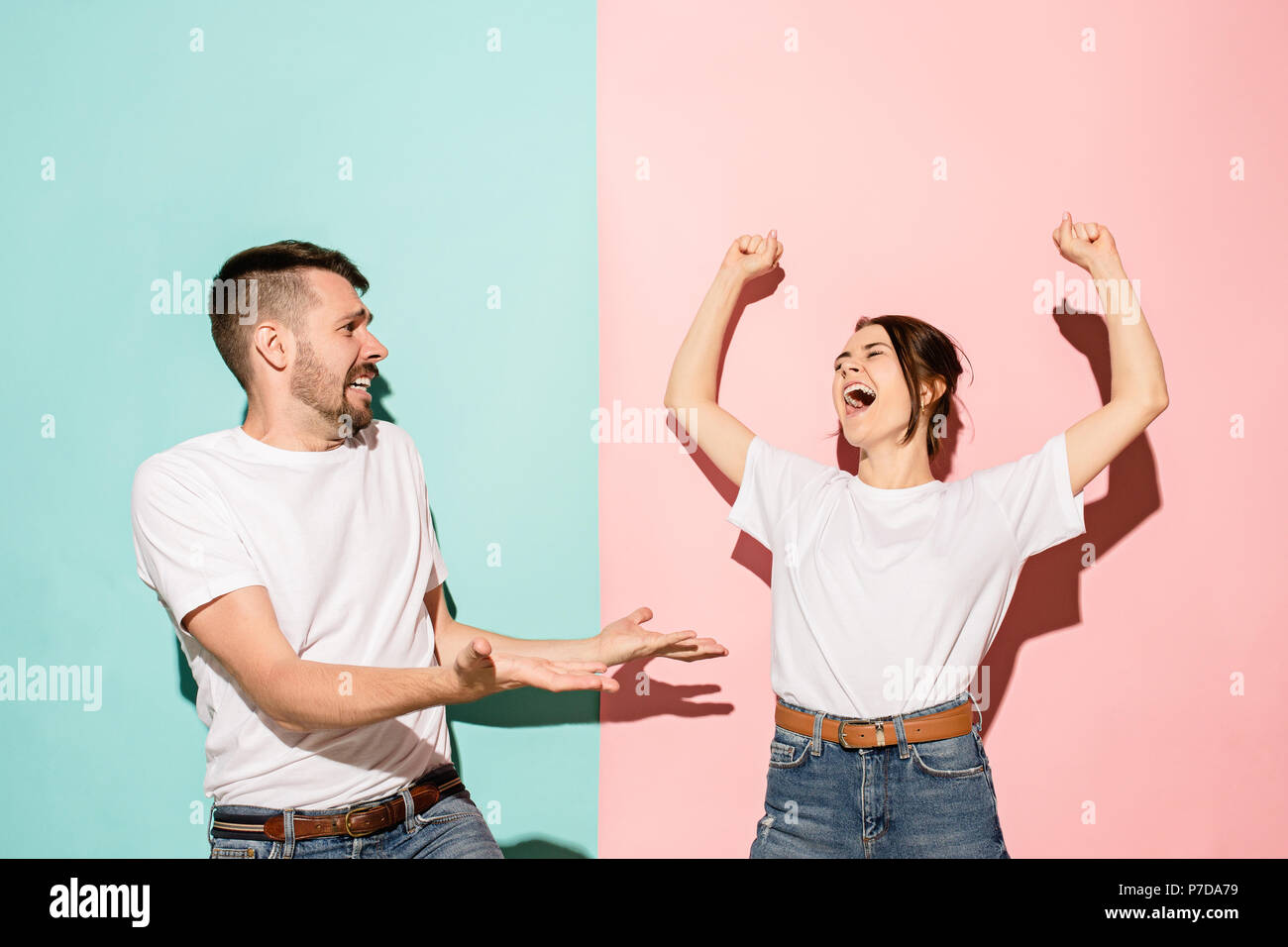 Closeup portrait of young couple, man, woman. One being excited happy smiling, other serious, concerned, unhappy on pink and blue background. Emotion contrasts Stock Photo