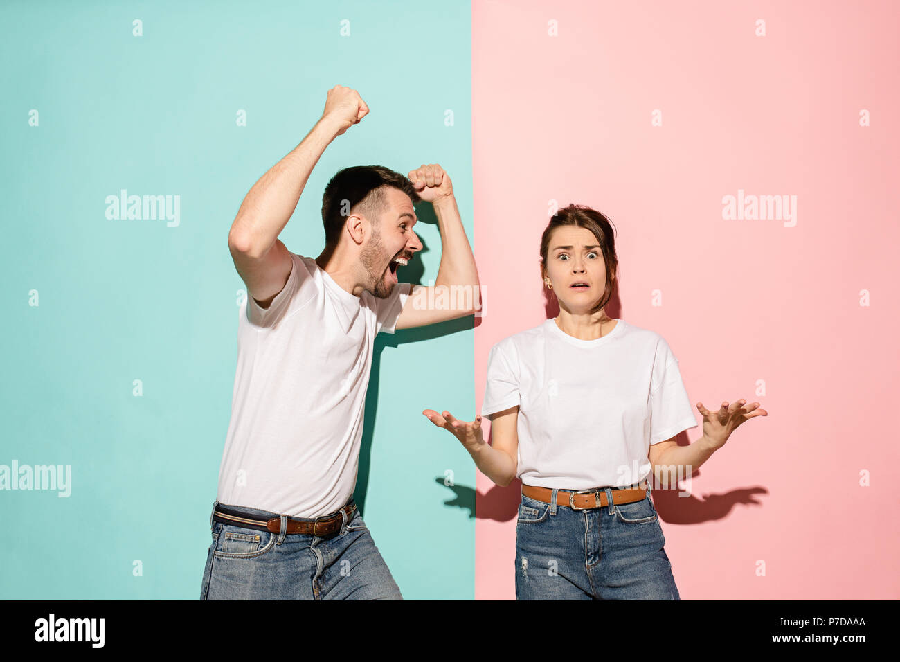 Closeup portrait of young couple, man, woman. One being excited happy smiling, other serious, concerned, unhappy on pink and blue background. Emotion contrasts Stock Photo