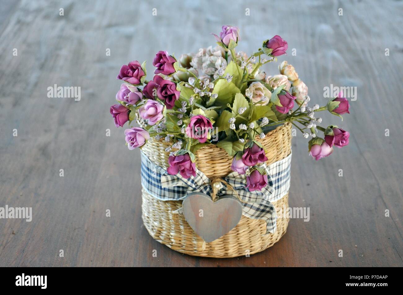 Basket with colorful mauve roses flowers, wrapped with a textile cloth and  a little symbolic heart in the middle, on brown wood background, copy space  Stock Photo - Alamy