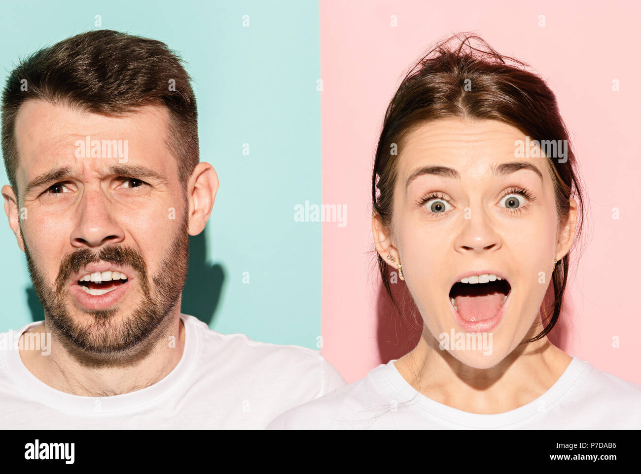 Closeup portrait of young couple, man, woman. One being excited happy smiling, other serious, concerned, unhappy on pink and blue background. Emotion contrasts Stock Photo