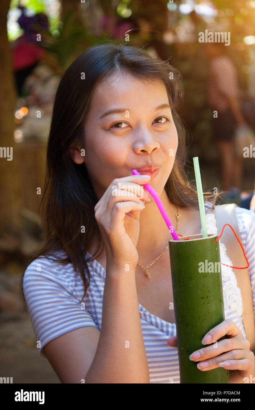 Young beautiful asian woman drinking Roselle juice from tube in a cup made of bamboo. Stock Photo