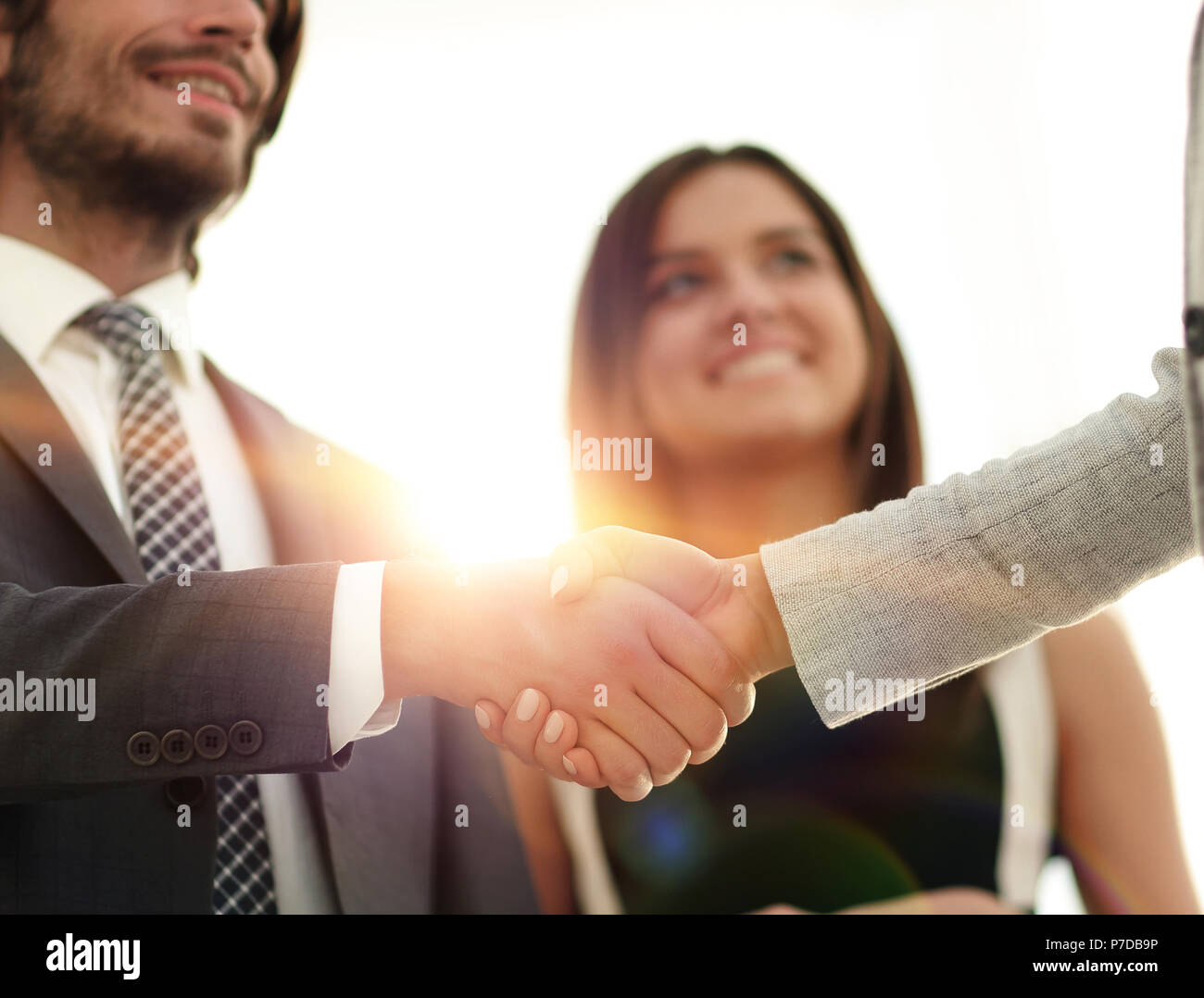 Businesspeople shaking hands against room with large window loo Stock