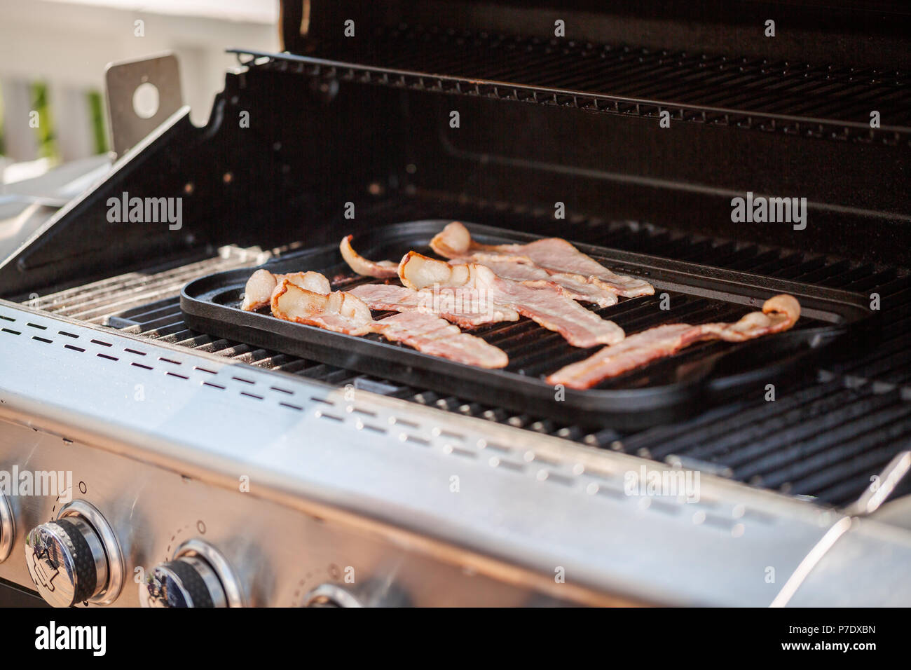 https://c8.alamy.com/comp/P7DXBN/grilling-bacon-strips-on-cast-iron-griddle-in-outdoor-gas-grill-P7DXBN.jpg