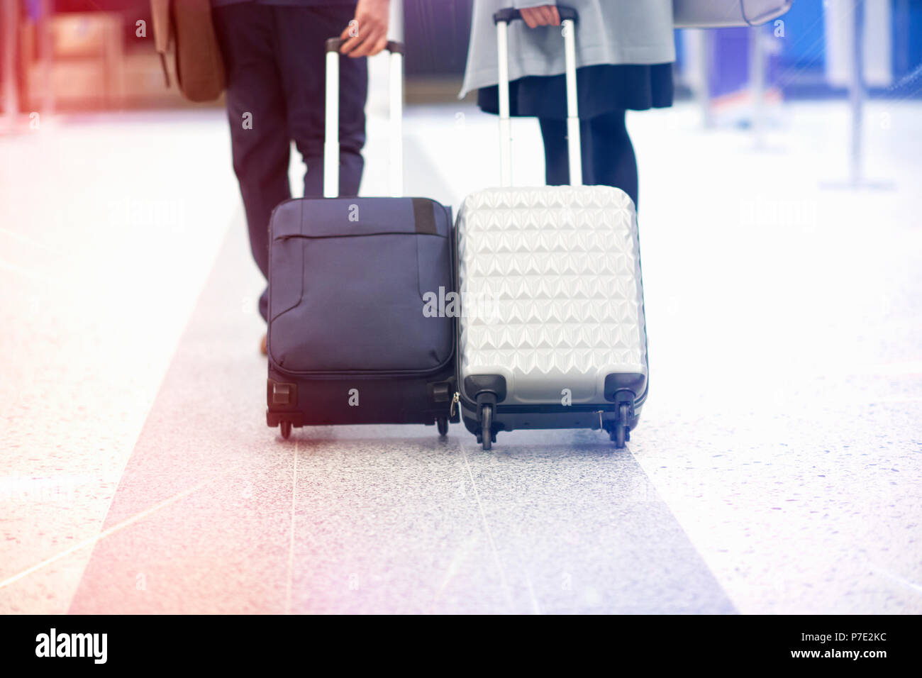 Businessman and businesswoman pulling wheeled suitcases, low section, rear view Stock Photo