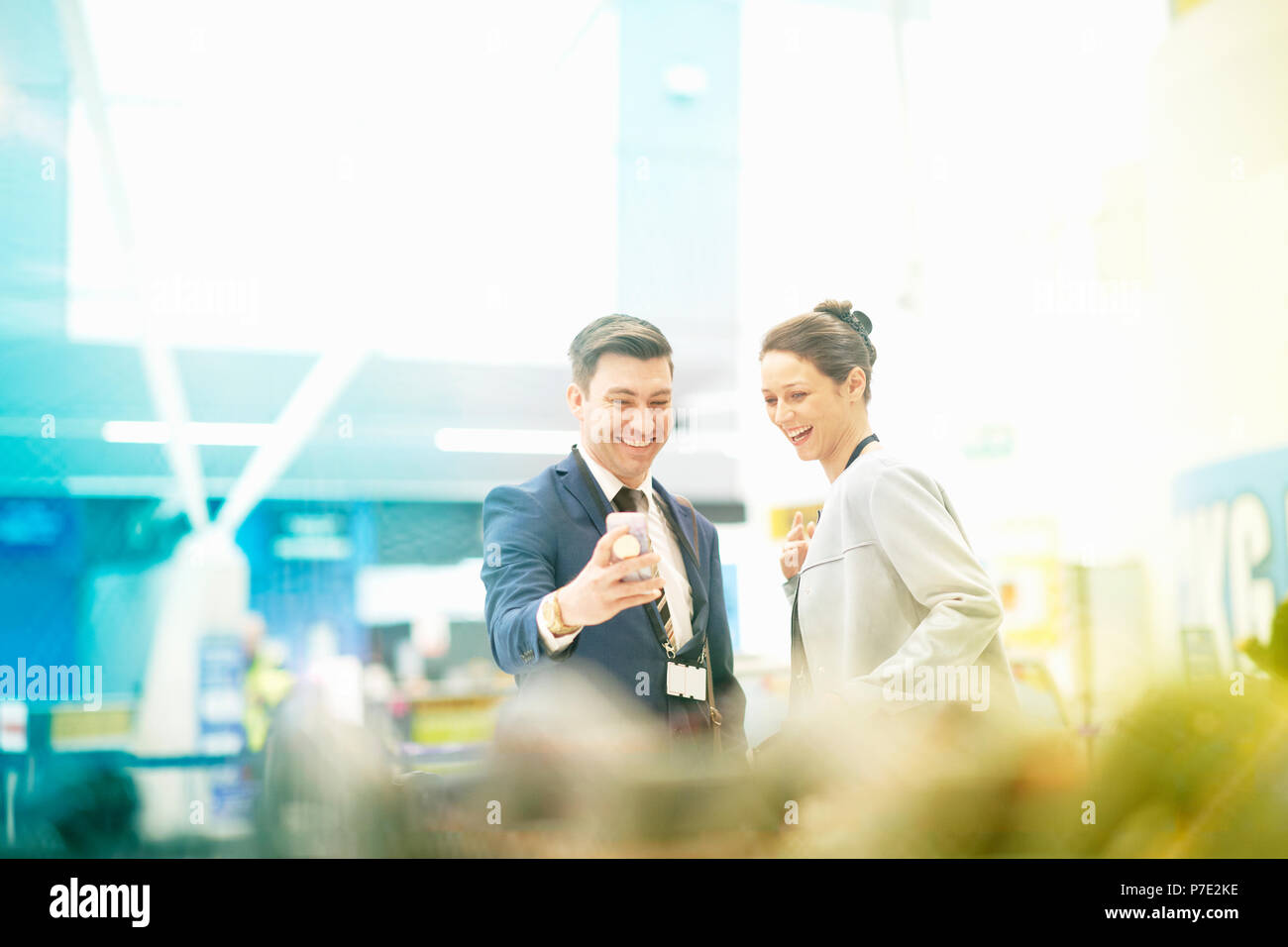 Businessman and businesswoman standing together, looking at smartphone, laughing Stock Photo