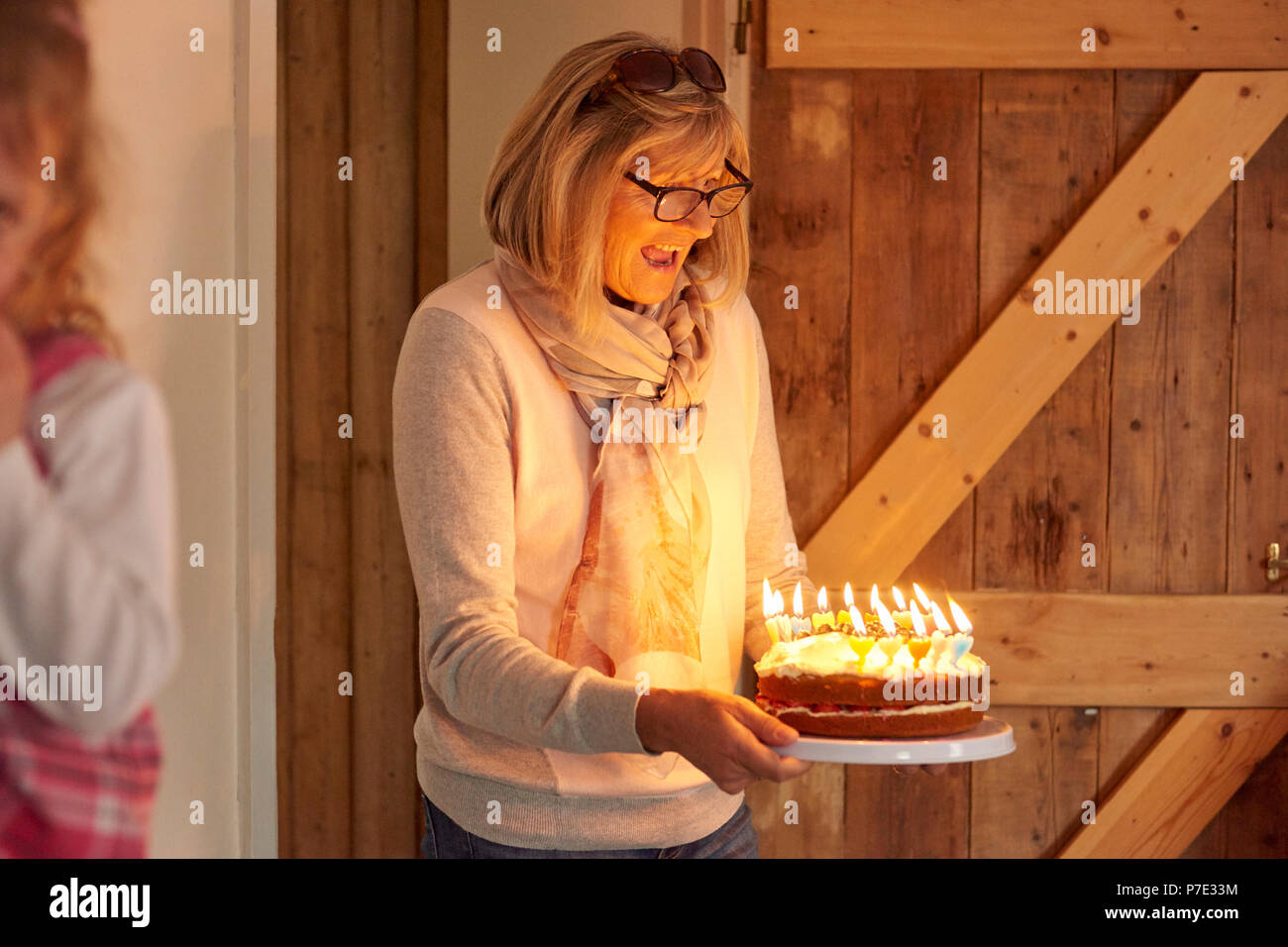 Senior woman carrying birthday cake with lit candles in kitchen Stock Photo