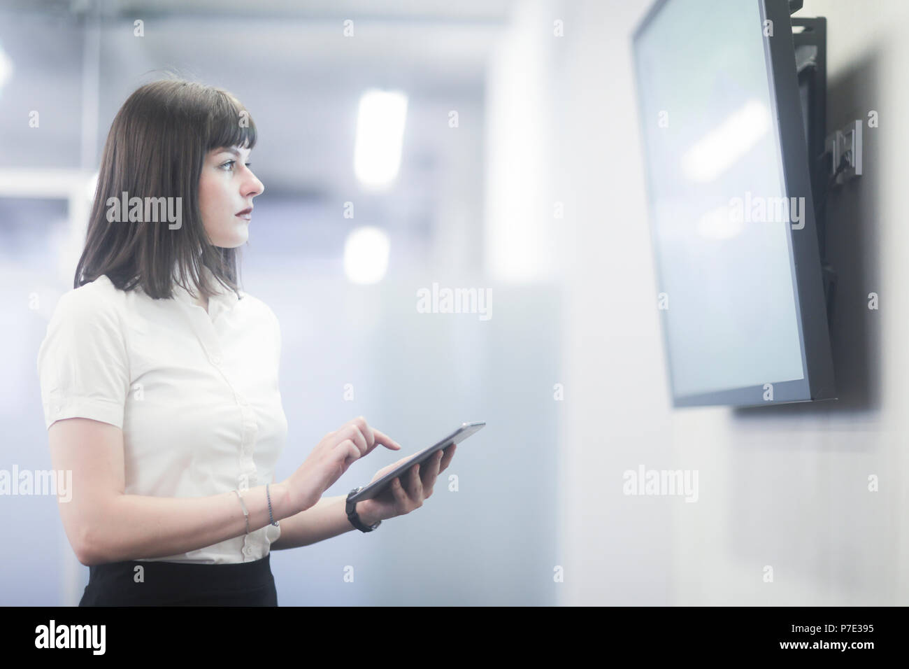 Businesswoman using digital tablet looking at tv Stock Photo