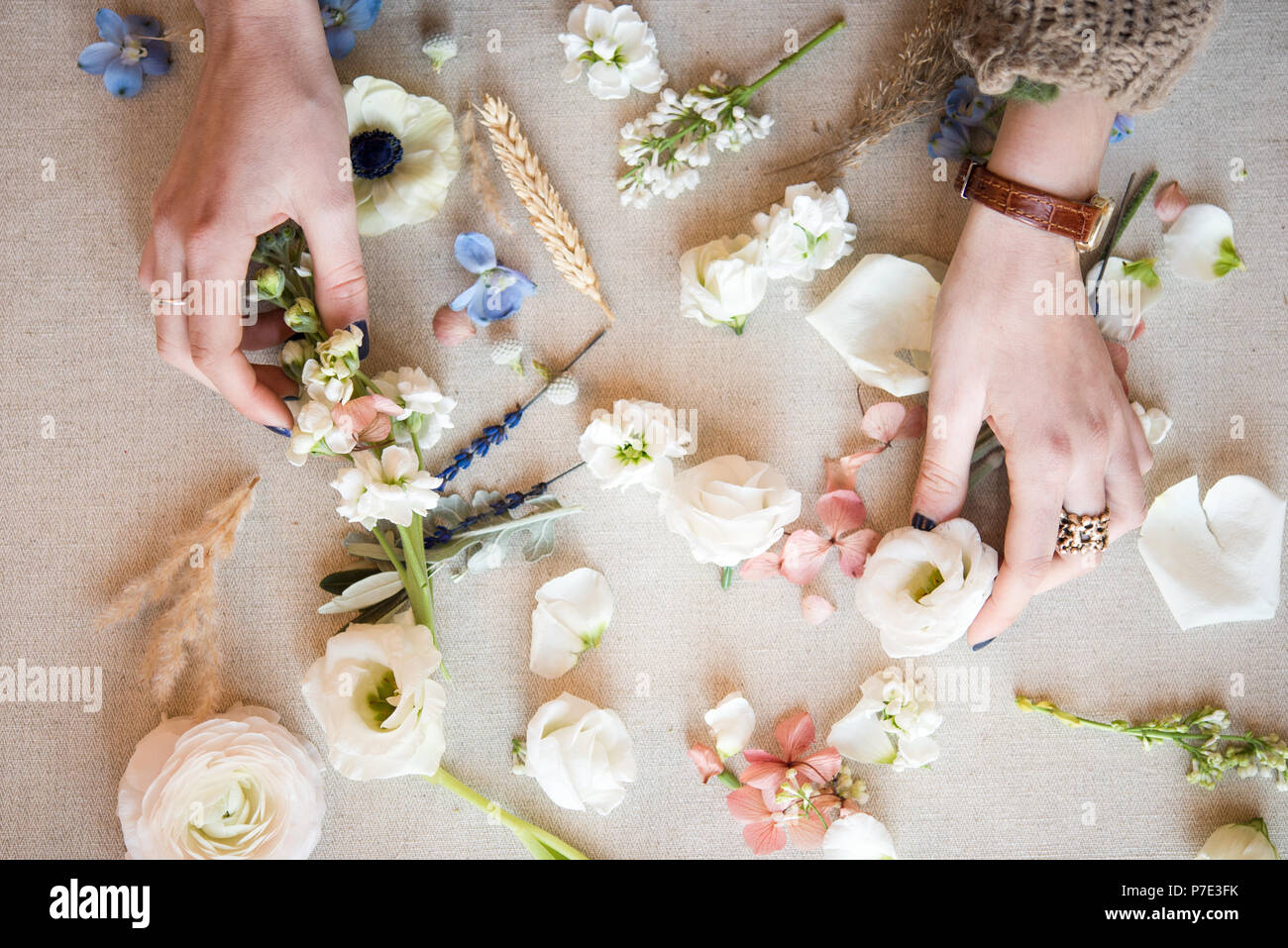 Woman arranging pastel flower heads and stems on textile, detail of hands, overhead view Stock Photo