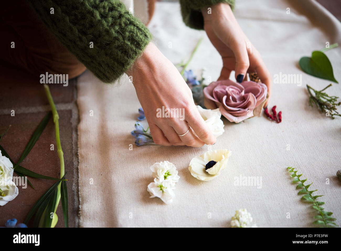 Woman arranging pastel flower heads and leaf stems on textile, detail of hands Stock Photo