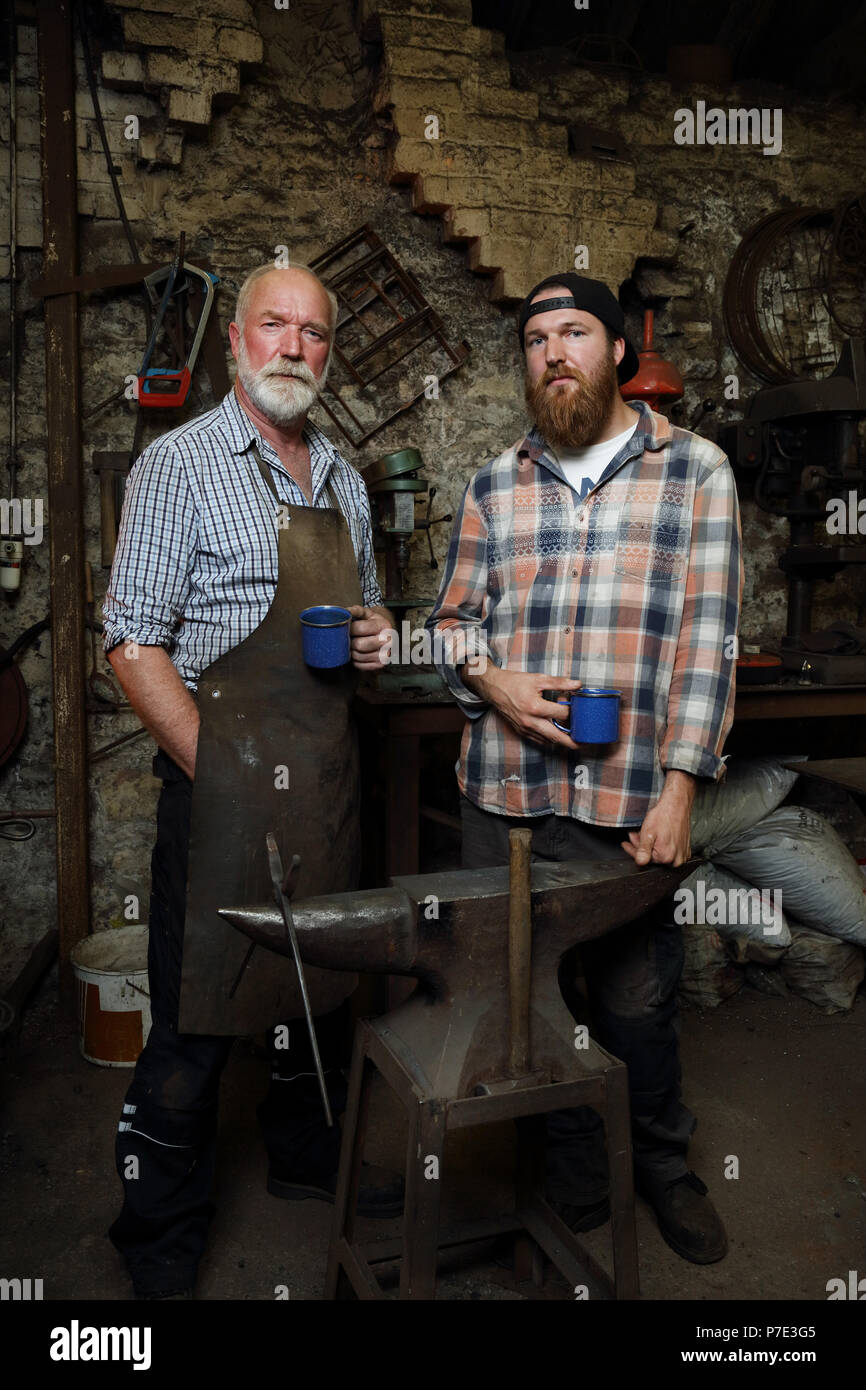 Senior blacksmith and son taking a break in blacksmiths shop, portrait Stock Photo