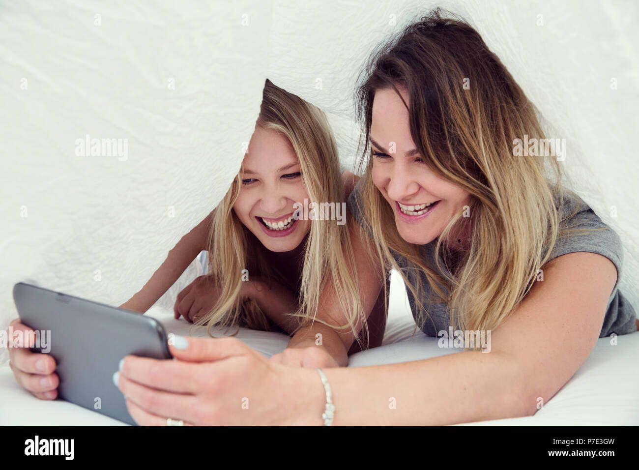 Friends underneath bed sheet using digital tablet smiling Stock Photo