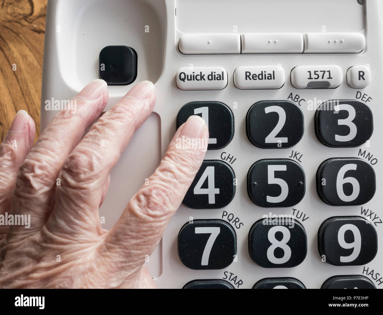 Visually impaired elderly woman dialling NHS 111 help line on big button telephone. Stock Photo