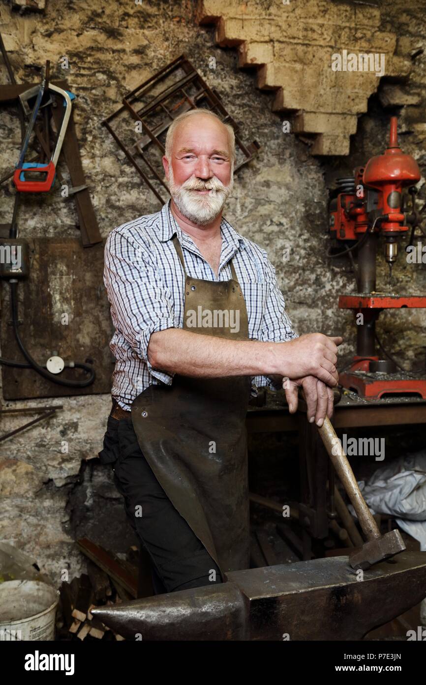 Blacksmith with hammer and anvil in blacksmiths shop, portrait Stock