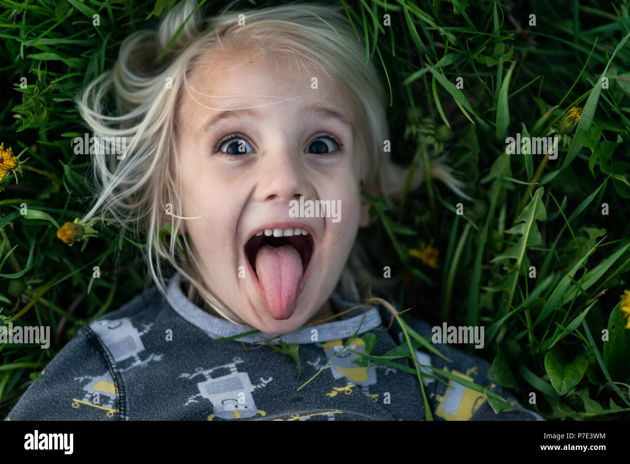 Blond haired boy lying on grass sticking tongue out, portrait Stock Photo
