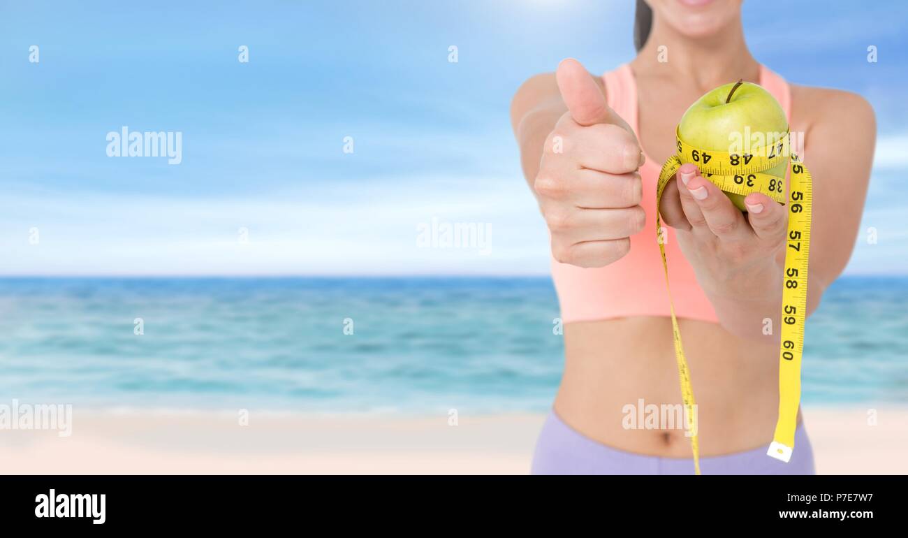 Woman measuring weight with measuring tape on waist and holding apple on Summer beach Stock Photo