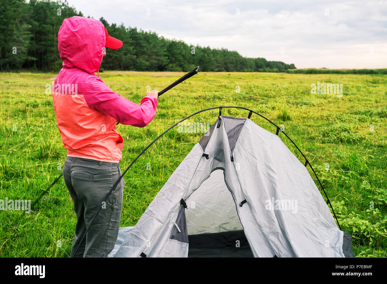 Girl in a pink jacket with a hood sets up a tent Stock Photo