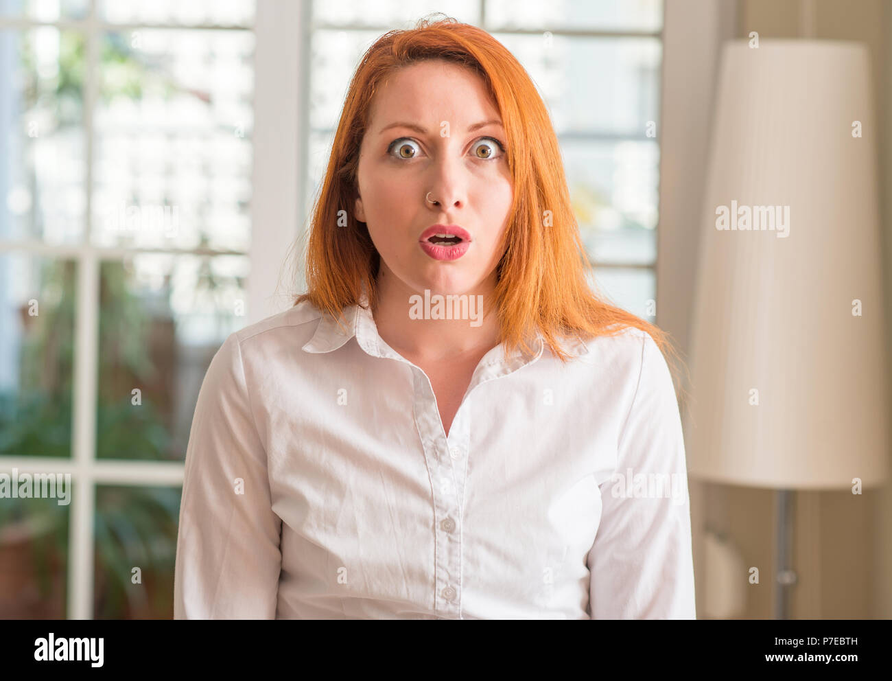Redhead Woman Wearing White Shirt At Home Scared In Shock With A