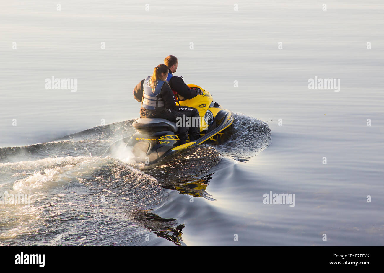 29 June 2018 A young couple on board a powerful Yamaha Jet-Ski as they head to sea from Groomsport Harbour Northern Ireland on a flat calm evening Stock Photo