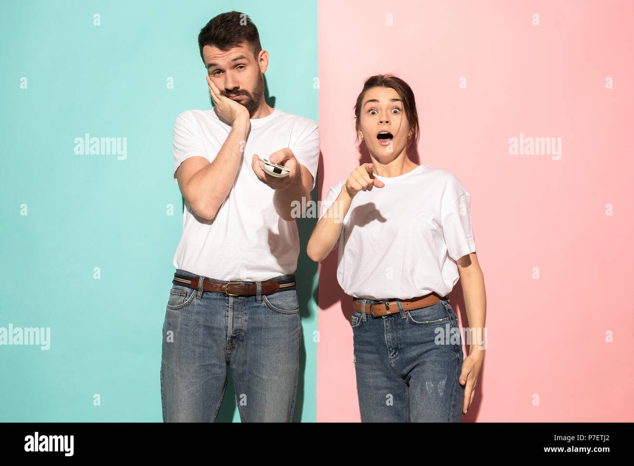 Closeup portrait of young couple, man, woman. One being excited happy smiling, other serious, concerned, unhappy on pink and blue background. Emotion contrasts Stock Photo