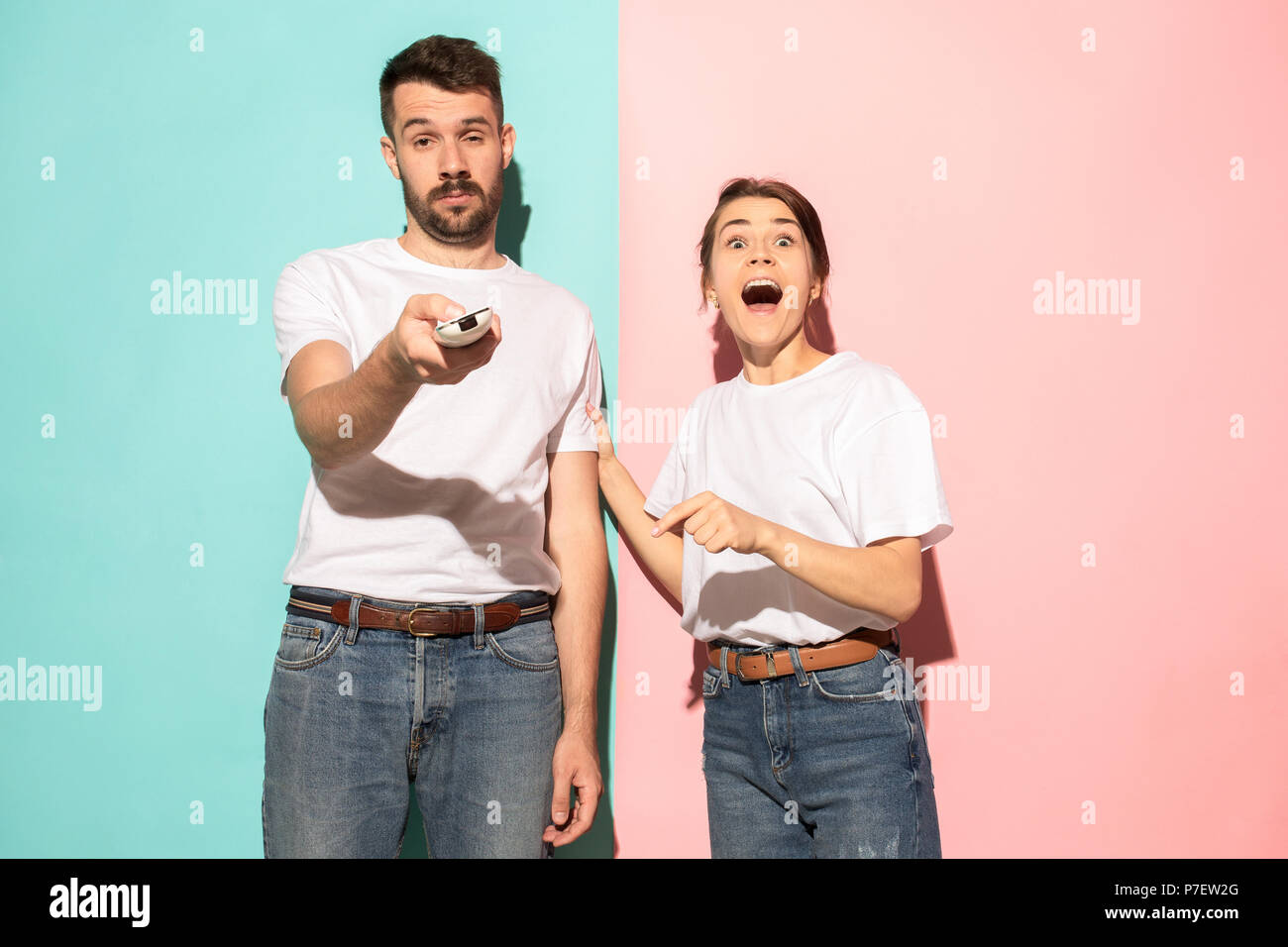 Closeup portrait of young couple, man, woman. One being excited happy smiling, other serious, concerned, unhappy on pink and blue background. Emotion contrasts Stock Photo