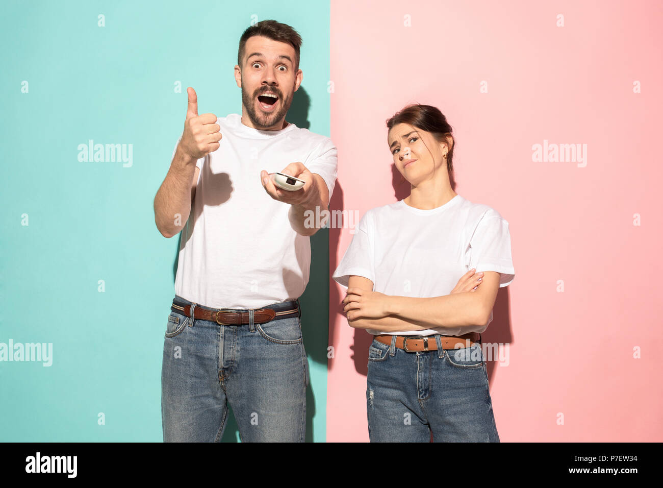 Closeup portrait of young couple, man, woman. One being excited happy smiling, other serious, concerned, unhappy on pink and blue background. Emotion contrasts Stock Photo