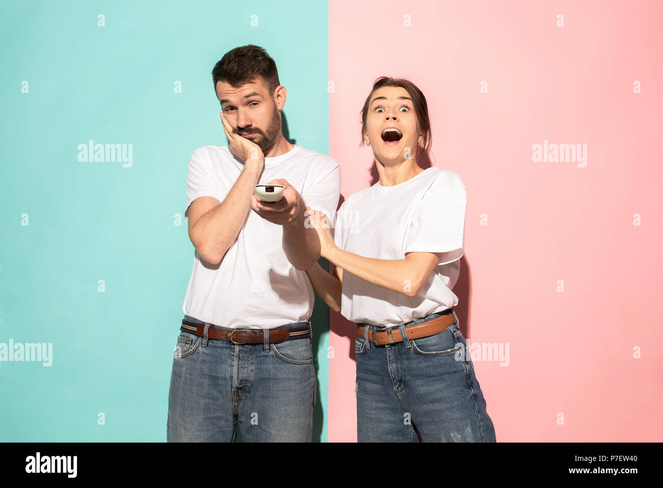 Closeup portrait of young couple, man, woman. One being excited happy smiling, other serious, concerned, unhappy on pink and blue background. Emotion contrasts Stock Photo