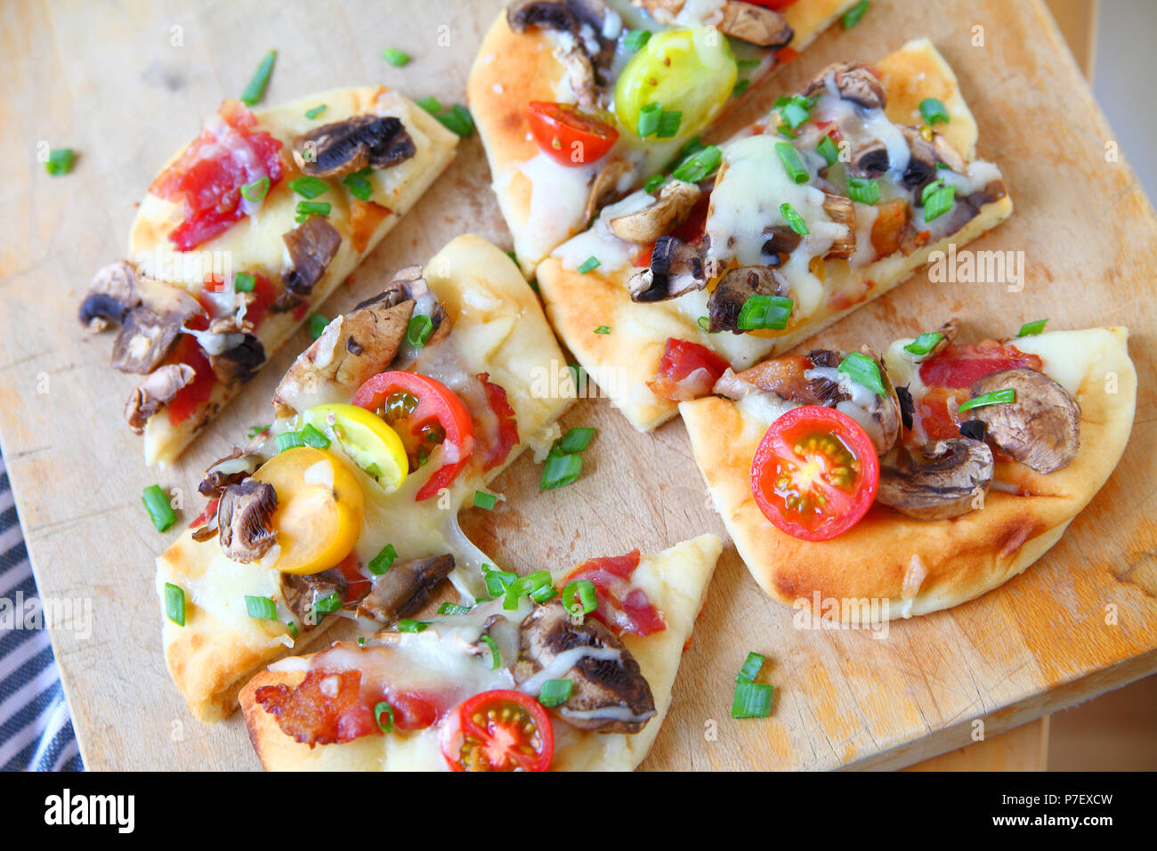 Overhead of small bacon, mushroom and cherry tomato pizzas cut into portions Stock Photo