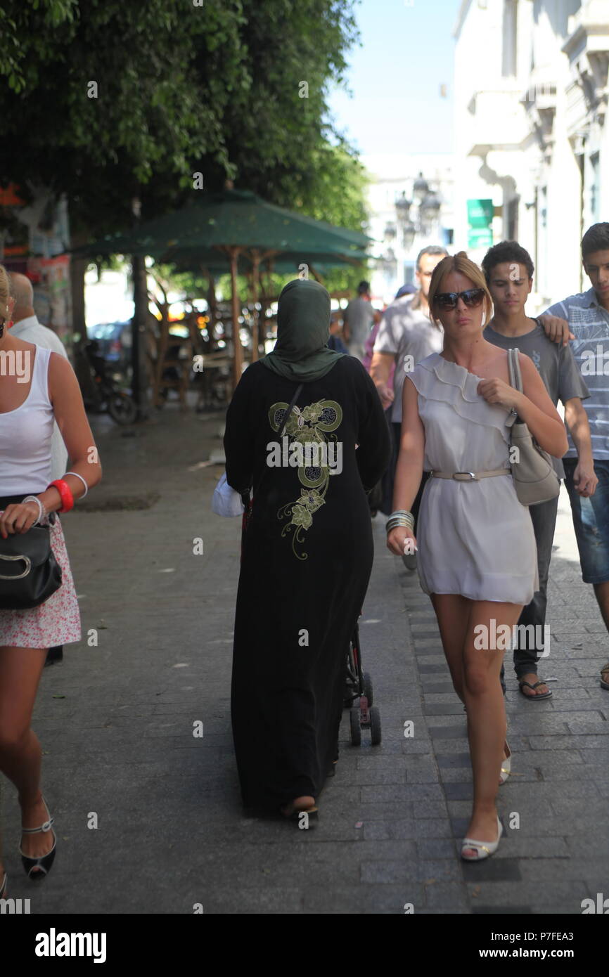 Muslim lady walking down the street in traditional dress in down town Tunis  as tourist visitors girls walking in mini-skirts and with open shoulders  Stock Photo - Alamy