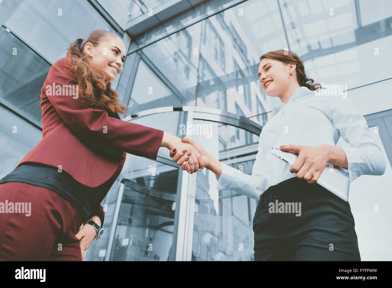 Handshake of two young girls against the background of a multi-storey office building. Make a deal. Friendly relations. Office staff. Stock Photo