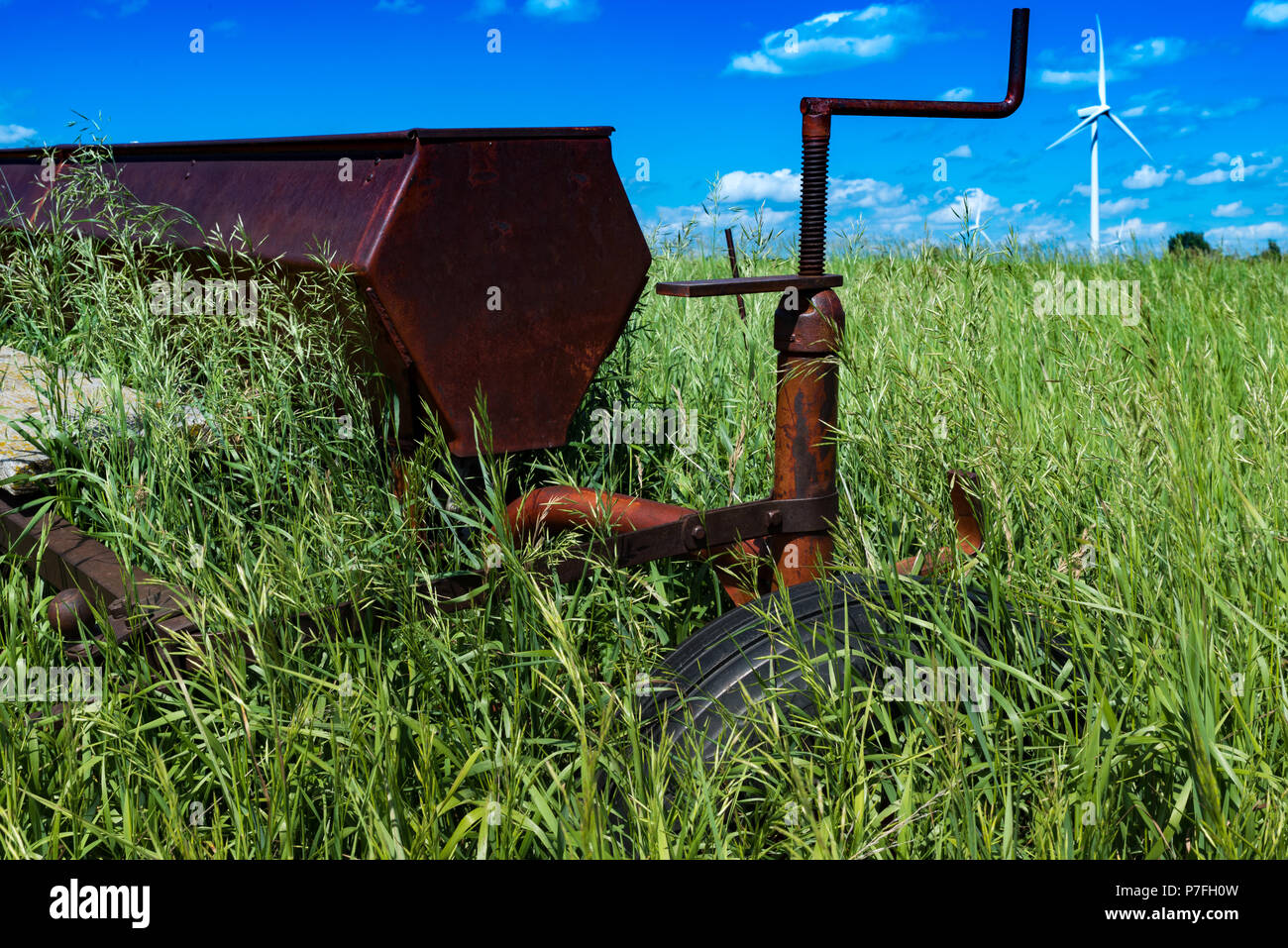 Vintage farming disc harrow in a field surrounded by tall grass with wind turbines outside of Swift Current, Saskatchewan, Canada Stock Photo