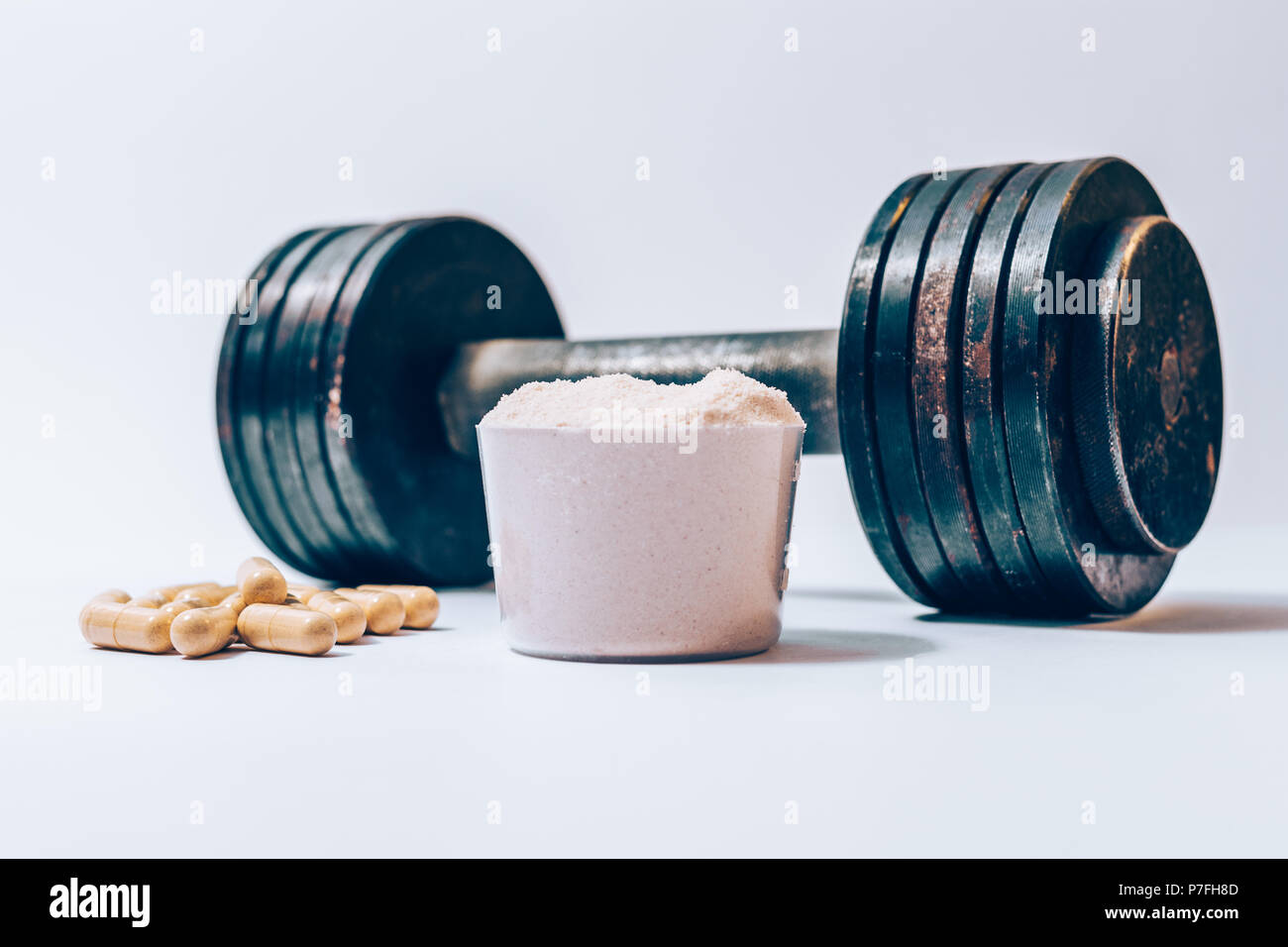 Whey protein powder in a scoop next to heap of vitamin pills and old rusty  dumbbell on a white background. Sports nutrition supplements and heavy weig  Stock Photo - Alamy