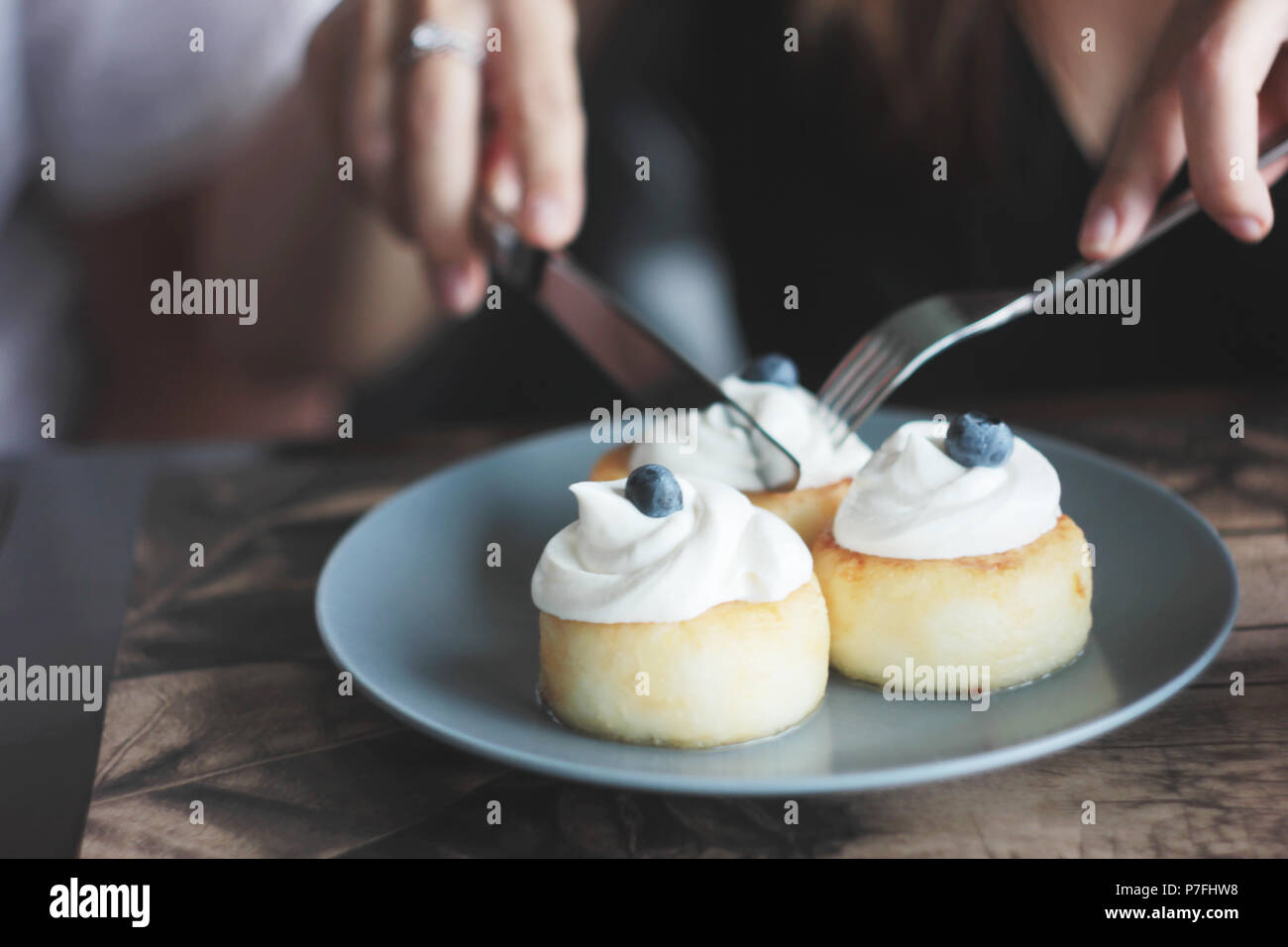 Cheesecakes with cream and blueberries on blue plate, women's hands with knife and fork Stock Photo