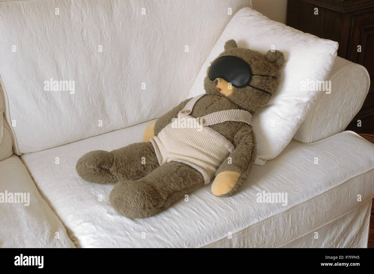 Teddy Bear lies with a sleeping mask on a couch, Germany Stock Photo