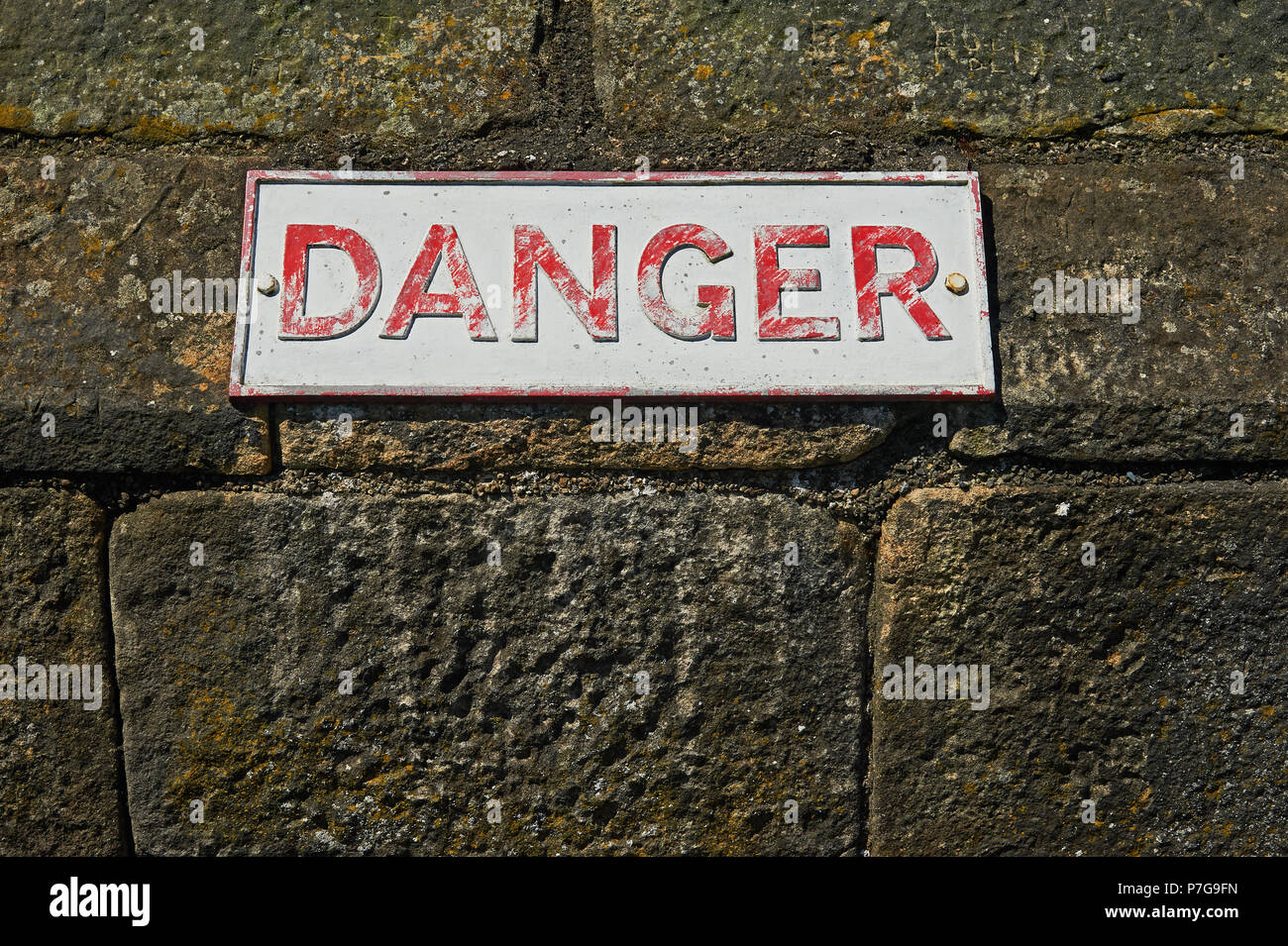 Metal plaque with the word DANGER on a stone wall Stock Photo