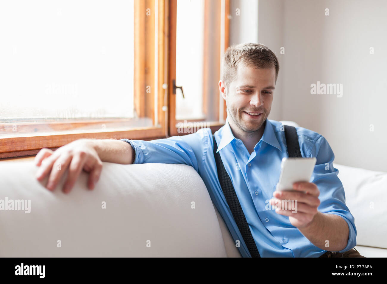 Handsome man sitting on sofa and texting from his smart phone Stock Photo