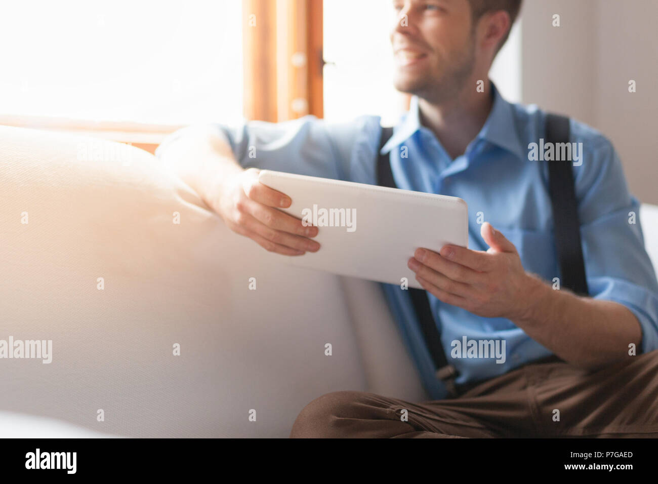 Handsome man sitting on sofa at home, using a digital tablet Stock Photo