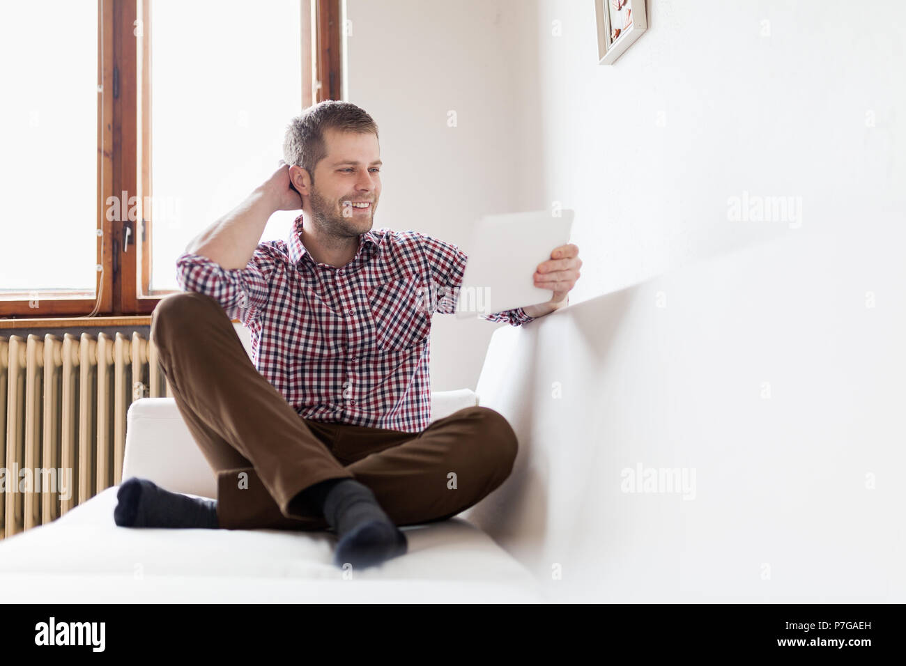 Handsome man sitting on sofa at home, using a digital tablet Stock Photo
