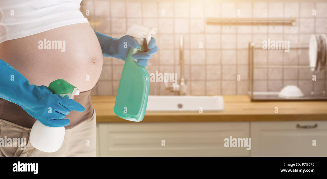 A pregnant woman wearing blue gloves cleaning the toilet Stock Photo