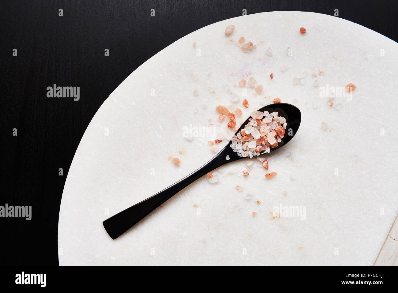 Flat lay, black spoon of pink himalayan salt on marble cutting board. Top view with copy space. Stock Photo