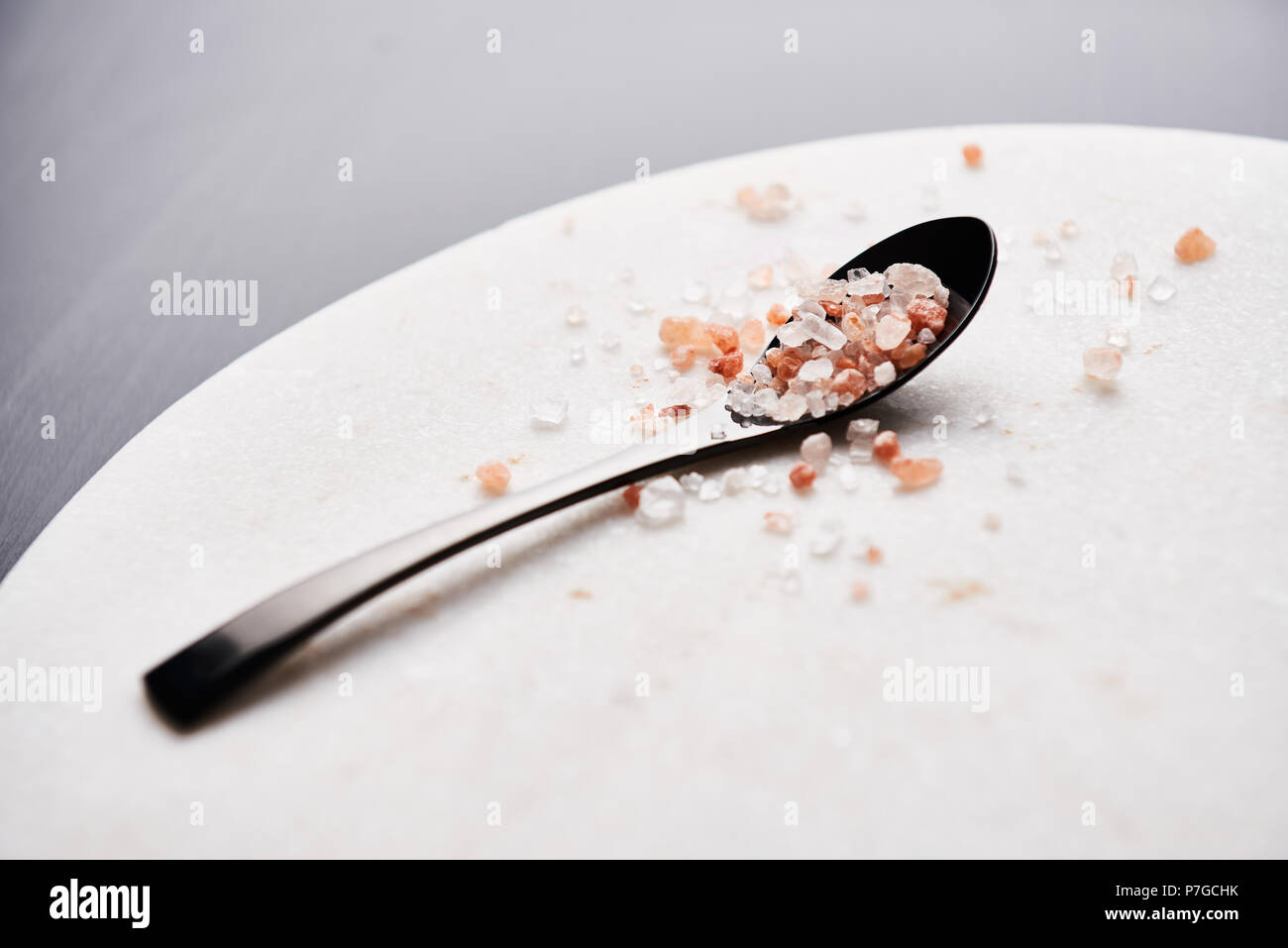 Black spoon of pink himalayan salt on marble cutting board with copy space. Stock Photo
