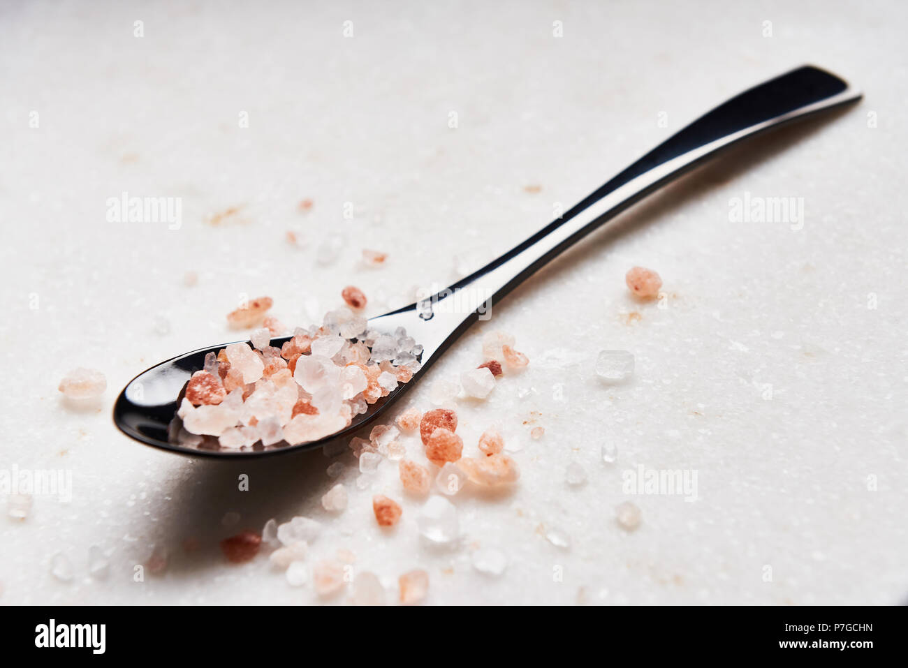 Black spoon of pink himalayan salt on marble table. Stock Photo